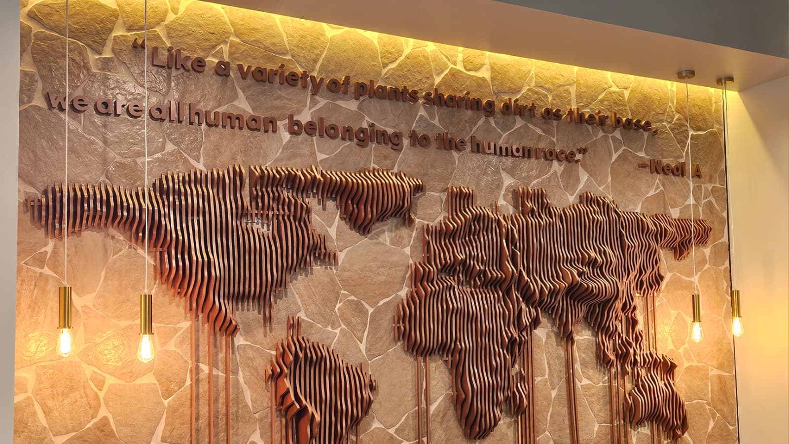 The world map wall inside Qurbah, carrying the founder's words in carved wood